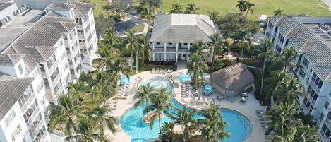 A hotel with a central pool, multiple balconies, and palm trees.
