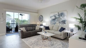 A spacious living room with a grey sofa, a white coffee table, and a large abstract painting on the wall. - CHOSEN BONITA'S FAVORITE and VRBO's PREMIER HOST with 85" TV and  2 KING BEDS! (Bonita Springs)