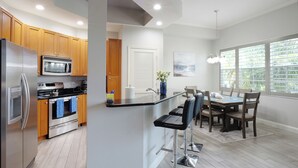 A modern kitchen with stainless steel appliances, wooden cabinets, and a bar area with stools. - CHOSEN BONITA'S FAVORITE and VRBO's PREMIER HOST with 85" TV and  2 KING BEDS! (Bonita Springs)