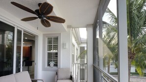 A spacious balcony with a ceiling fan, a sofa, a coffee table with a plant, and a view of palm trees. - CHOSEN BONITA'S FAVORITE and VRBO's PREMIER HOST with 85" TV and  2 KING BEDS! (Bonita Springs)
