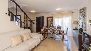 A living room with a sofa, a dining table with chairs, a staircase, and a TV on a cabinet. - El Campanario El Bosque by Ruralidays (Cádiz)