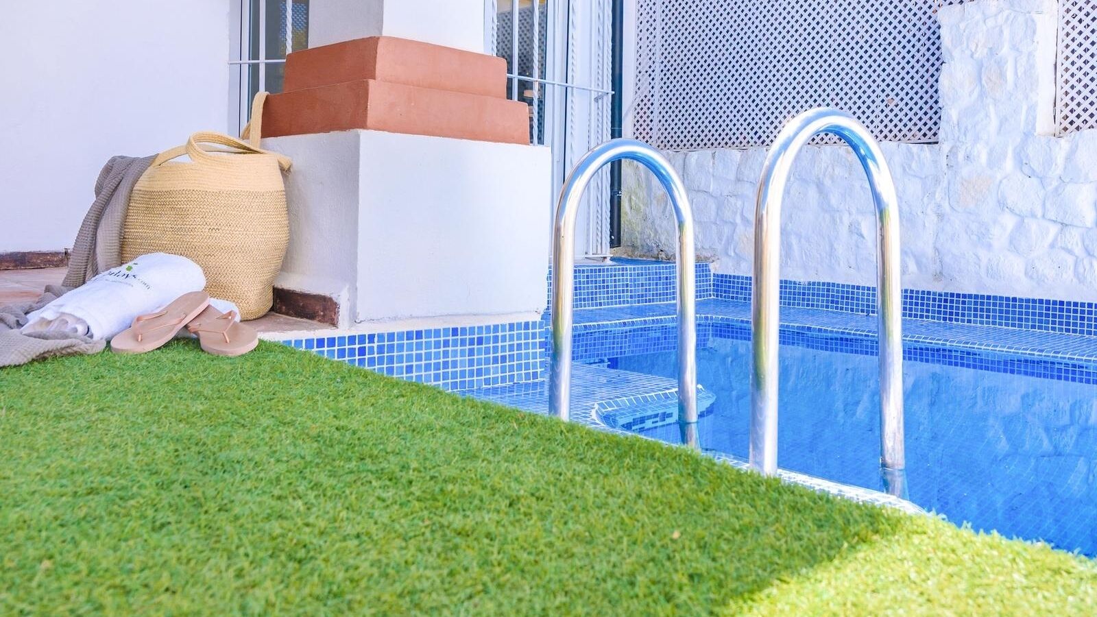 A swimming pool with clear blue tiles, a metal ladder, and a grassy area in front.