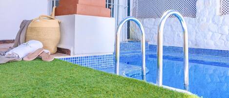 A swimming pool with clear blue tiles, a metal ladder, and a grassy area in front.