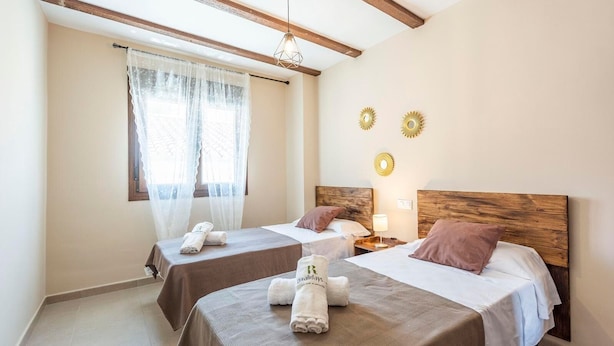 Une chambre d’hôtel avec deux lits, une fenêtre avec des rideaux légers et des appliques murales décoratives.