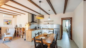 Une cuisine moderne avec un îlot central, des poutres en bois au plafond et un coin repas comprenant une table et des chaises.