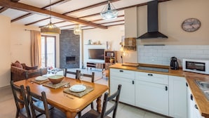 Une cuisine chaleureuse avec une table à manger en bois, des placards blancs et une cheminée en pierre.