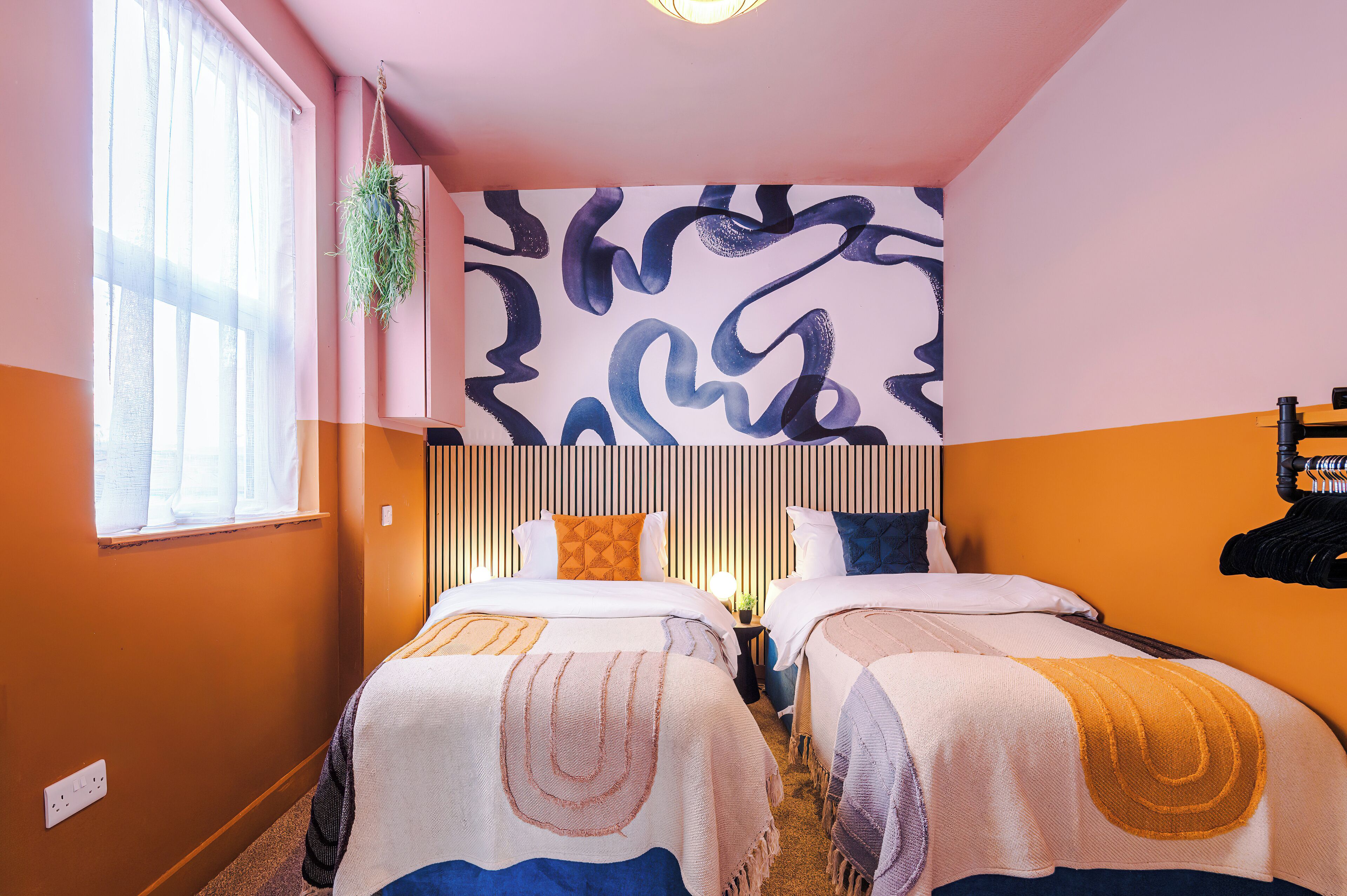 Ein Hotelzimmer mit zwei Betten, einem großen abstrakten Wandbild und einem Fenster mit durchsichtigen Vorhängen.