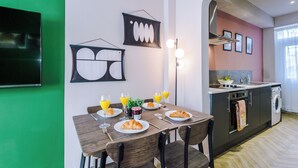 A modern kitchen with a dining area, featuring a wooden table, chairs, and a TV mounted on the wall. - Modern 4-Bedroom in Manchester (Salford)