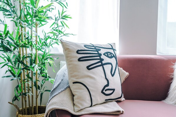A room with a red sofa, a beige pillow with a black design, and a bamboo plant in a woven basket.