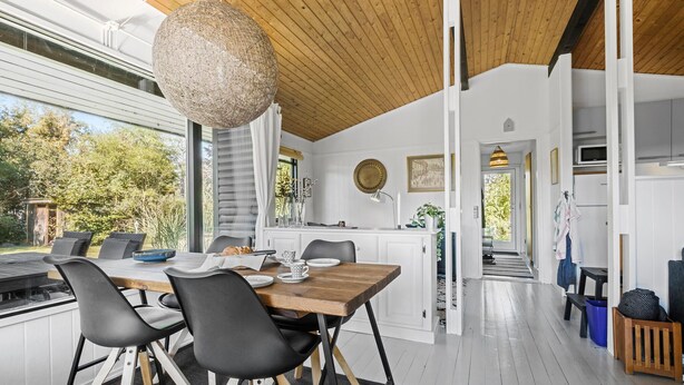 A modern kitchen with white cabinetry, a wooden ceiling, and a dining area with a large table and black chairs.