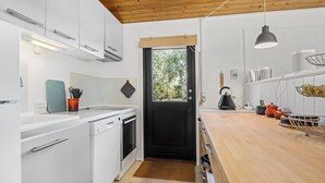 A modern kitchen with white cabinets, a black door, a wooden ceiling, and a wooden countertop.