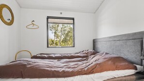 A bedroom with a bed, a window with a view of trees, a round mirror, and a wooden hanger.