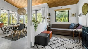 A modern living room with a wooden ceiling, large windows, a sofa, a dining table, and a fireplace.