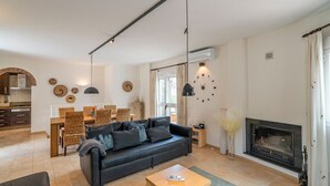 Een moderne woonkamer met een zwarte leren bank, een eethoek met rieten meubels en een open haard.