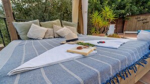 Een bed met een blauw-witte streepdeken, meerdere kussens en een boek en zonnebril erop.