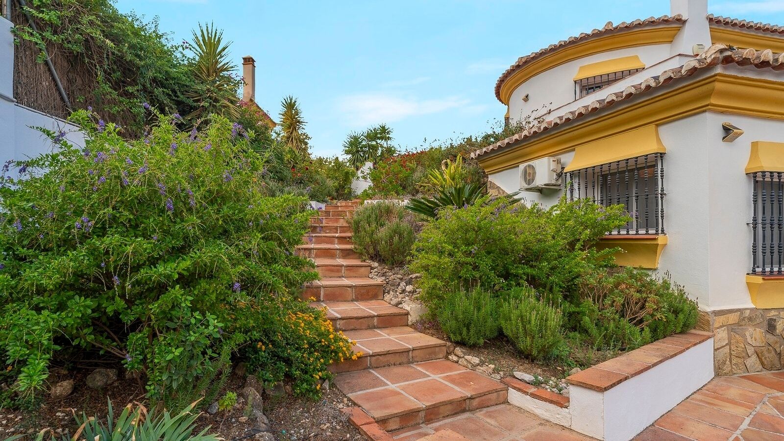 Eine Treppe führt zu einem Gebäude mit gelber Fassade, umgeben von üppiger Vegetation.