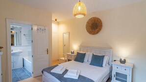 Een slaapkamer met een bed, nachtkastjes, een hanglamp, een spiegel en een deur naar de badkamer.