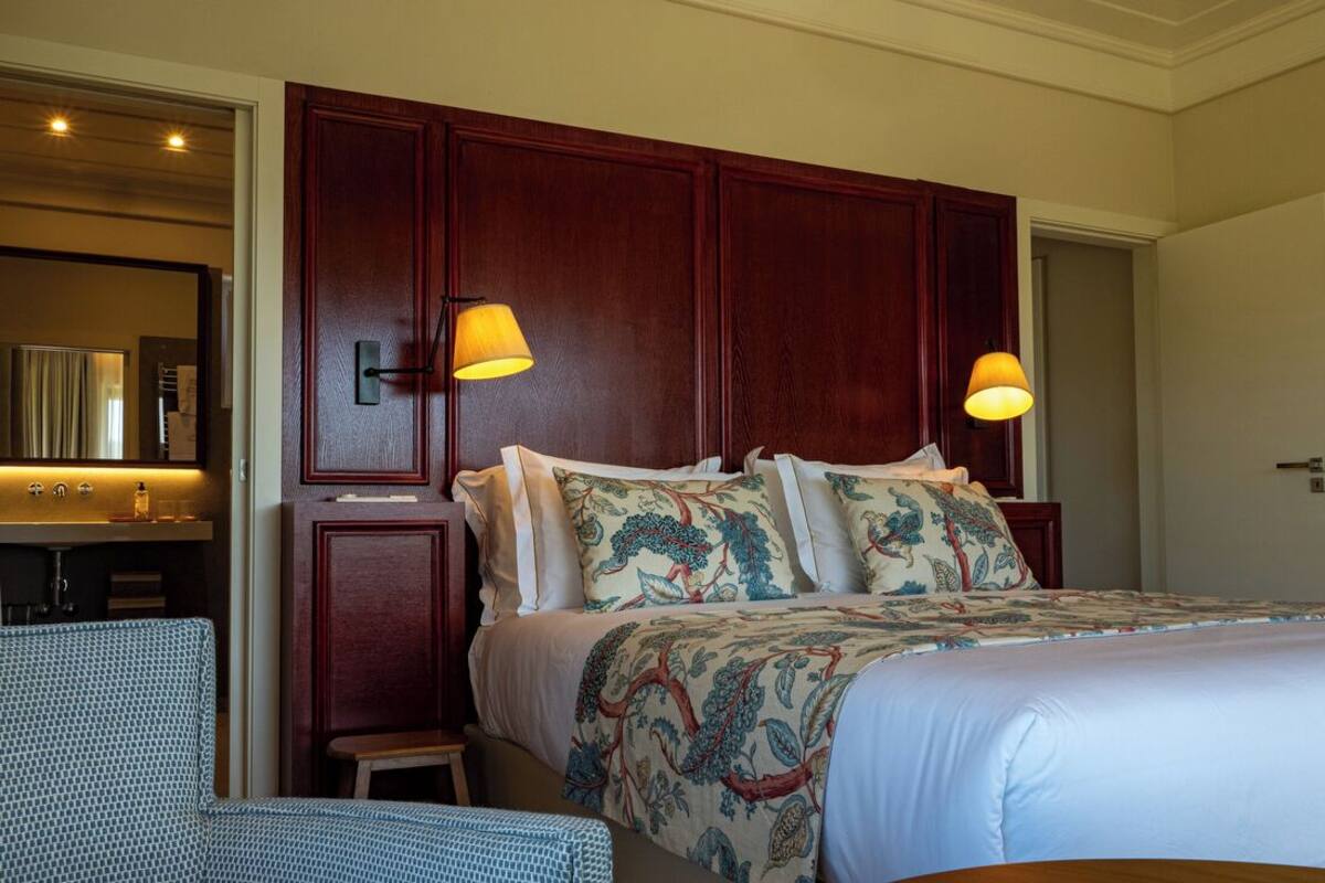 A hotel room with a large bed, two bedside lamps, a wooden headboard, and a small table.