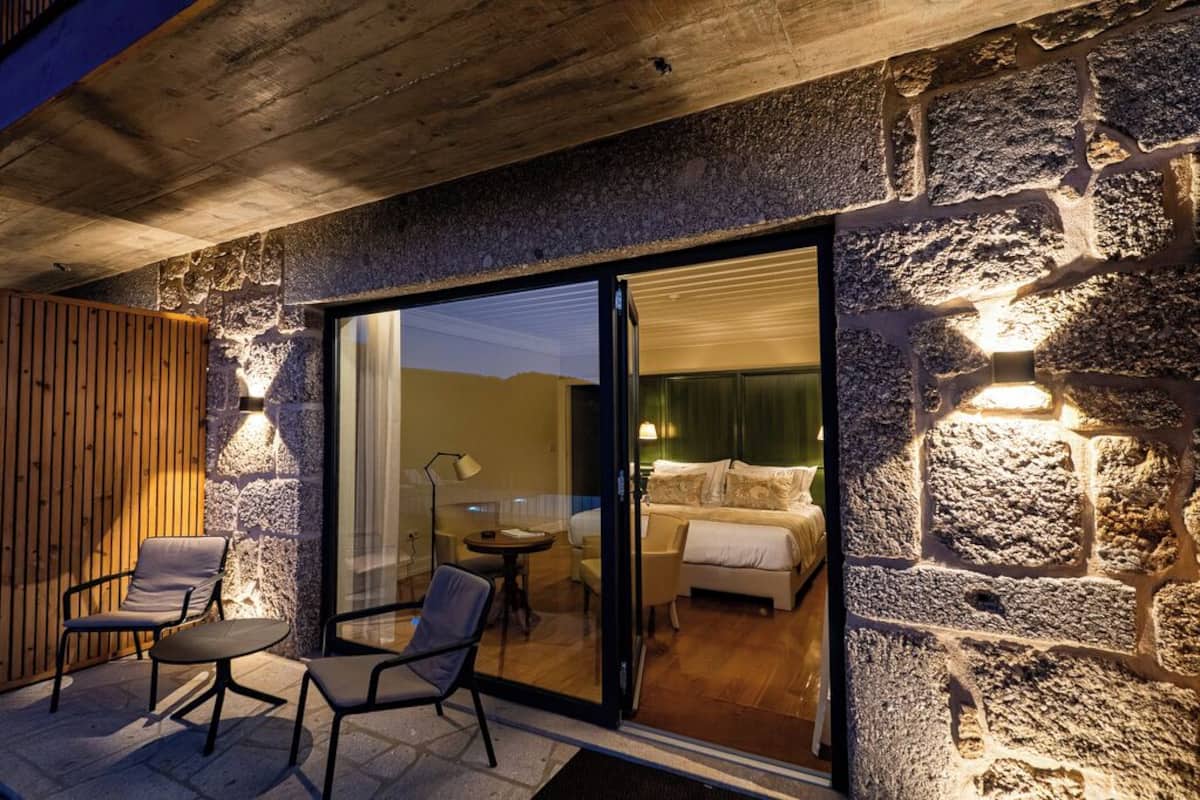 A modern room with a stone wall, a wooden slatted wall, and a glass door leading to a bedroom with a bed and a nightstand.