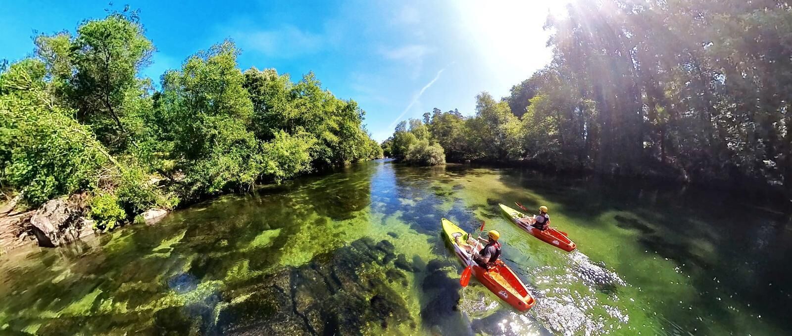 A river with kayaks and dense greenery on both sides.