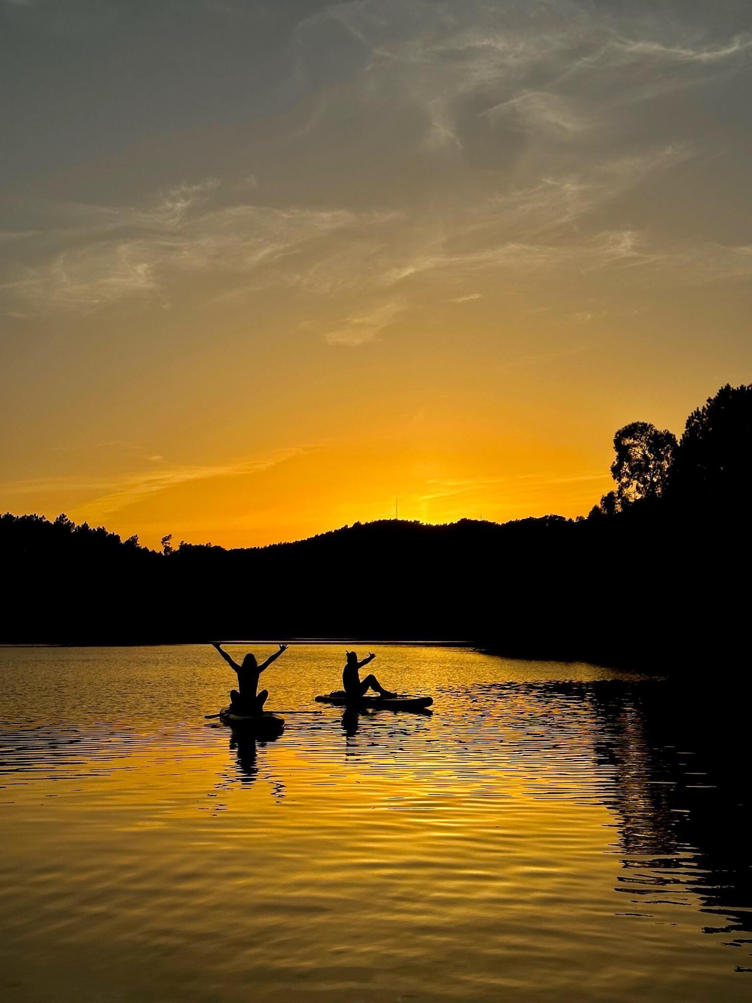 Un atardecer sobre un lago tranquilo con siluetas de personas en tablas de remo.