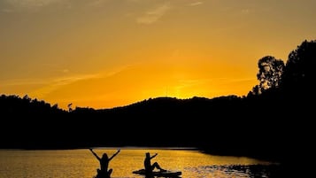 Un atardecer sobre un lago tranquilo con siluetas de personas en tablas de remo.