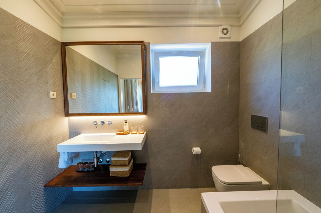 A modern bathroom with a built-in sink, a mirror, a small window, and a shower area.