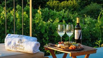 Une table avec une bouteille de vin, deux verres et un plateau de nourriture, le tout disposé sur un fond de verdure luxuriante.