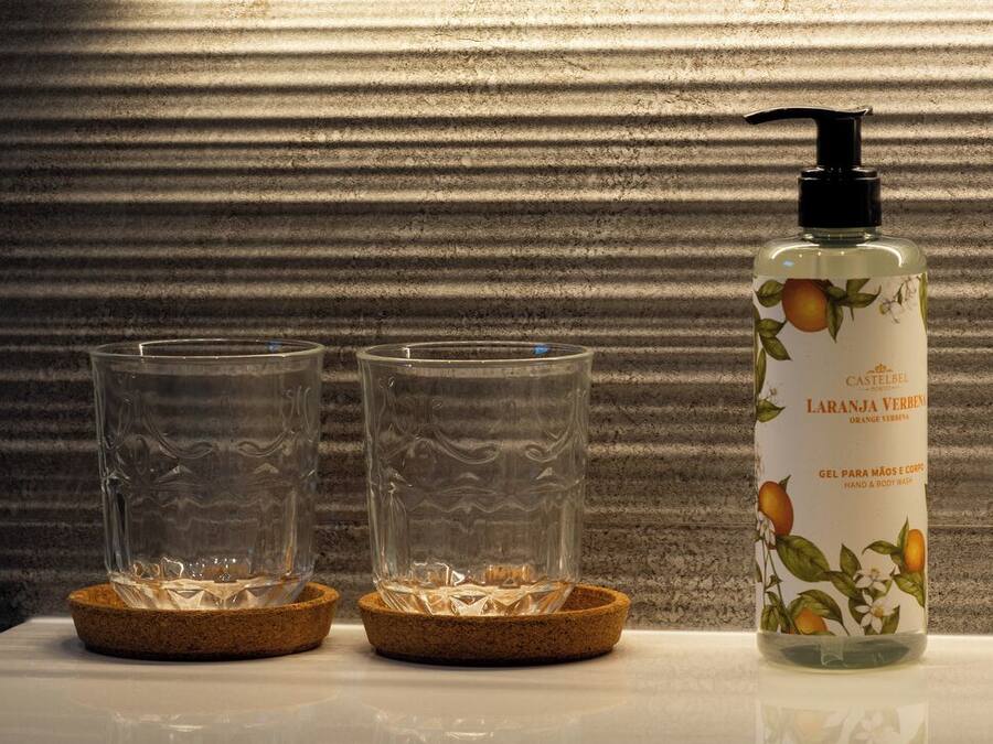 Una botella de jabón de manos y cuerpo Castelbel con dispensador, dos vasos vacíos sobre una mesa con posavasos de corcho.