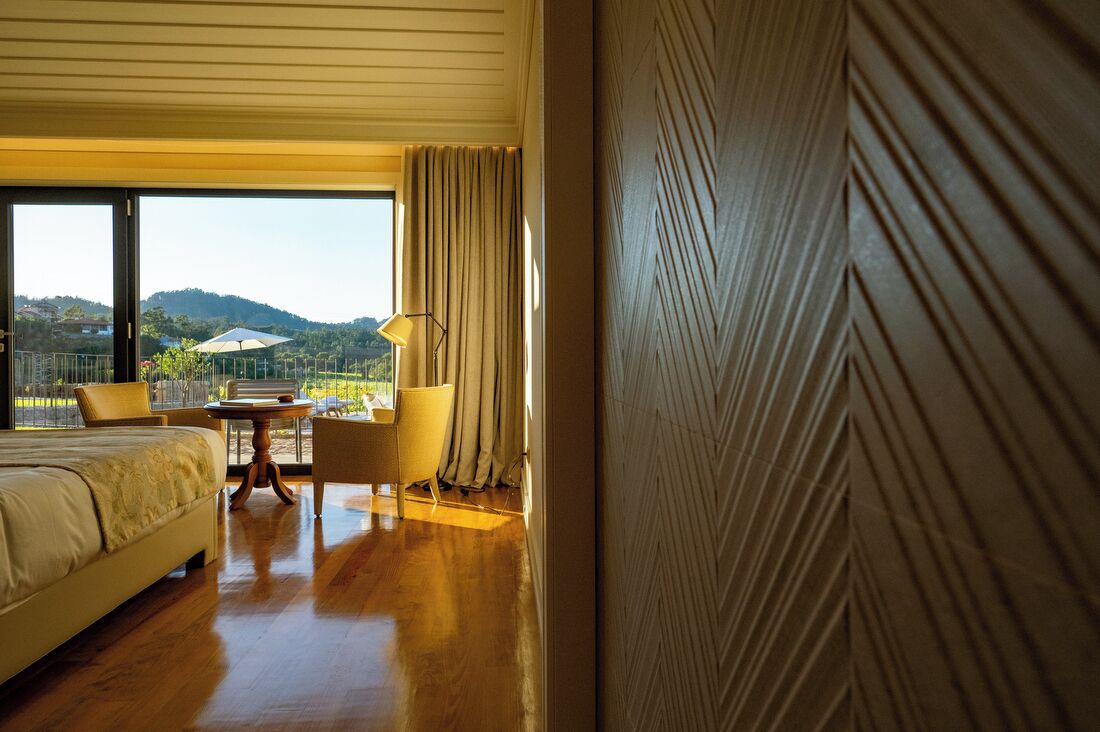 A hotel room with a bed, a table, a chair, and a view of the outdoors.