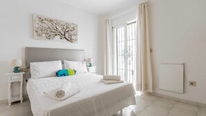 A bedroom with a bed, white curtains, a radiator, and a wall art piece. - Casa Jerez 14 en Nerja  by Ruralidays (Málaga)