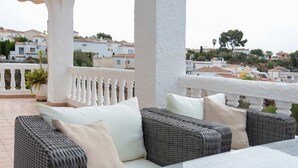 A balcony with wicker furniture and white cushions, overlooking a residential area with houses and trees. - Casa Jerez 14 en Nerja  by Ruralidays (Málaga)
