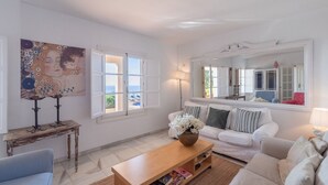 A living room with a white sofa, a wooden coffee table with a vase, a painting on the wall, and a window with a view of the sea. - Finca Kriek Rincón de la Victoria by Ruralidays (Málaga)