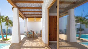 An outdoor patio with a table and chairs, a wooden door, and a pool. - Turqueta Chiclana de la Frontera by Ruralidays (Cádiz)