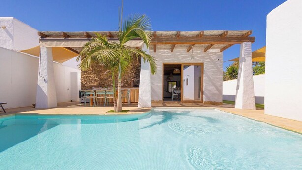A pool area with a pergola, a palm tree, and a stone wall. - Turqueta Chiclana de la Frontera by Ruralidays (Cádiz)