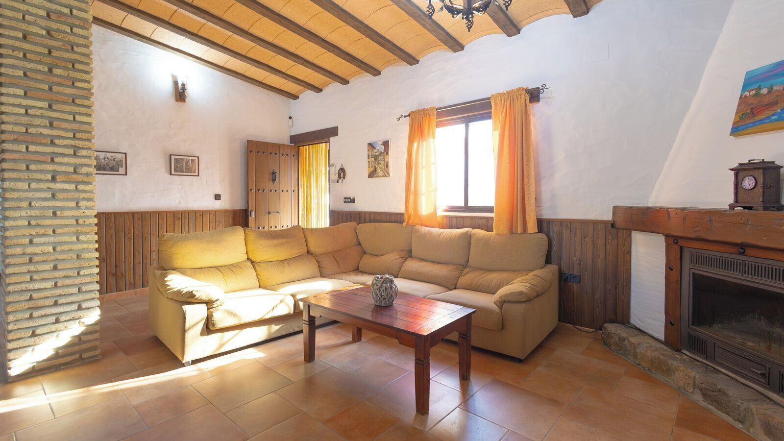 Una sala de estar acogedora con techo de madera, chimenea y un ventanal con cortinas.