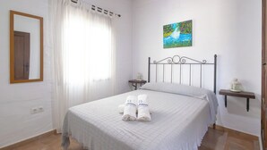Ein ordentlich bezogenes Bett mit weißer Bettdecke und zwei sauber gefalteten Handtüchern. Darüber an der Wand hängt ein Landschaftsbild.