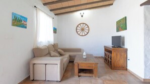 Ein Wohnzimmer mit beiger Couch, Couchtisch aus Holz, Fernseher auf einem Holzschrank und einem an der Wand befestigten Holzwagen.
