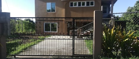 Una casa de dos pisos con techo rojo, entrada protegida por una reja y una escalera que lleva al nivel superior.