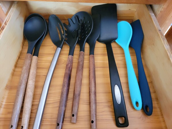 Eine Schublade mit verschiedenen Küchenutensilien, mit Holzgriffen und schwarzen sowie blauen Silikongriffen.