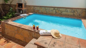A swimming pool with a stone wall, two drinks, and a towel with a hat. - Casa V. Escutia Torrox by Ruralidays (Málaga)