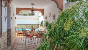 Une terrasse avec une table ronde et des chaises, un luminaire suspendu et une vue sur une piscine intérieure.
