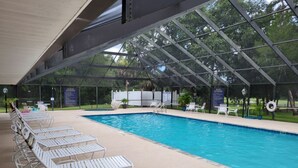 A covered swimming pool with lounge chairs and a pergola structure.