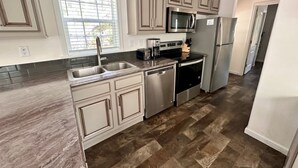 A modern kitchen with beige cabinetry, stainless steel appliances, and a herringbone-patterned floor.