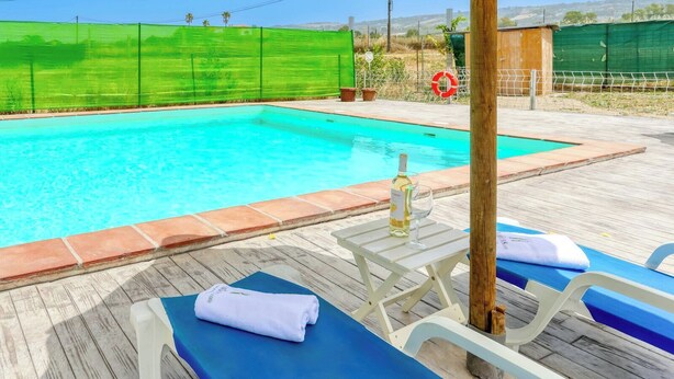 Una piscina con cubierta de madera, sillas de descanso y una botella de vino.