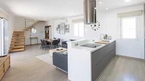 Una cocina moderna con una isla central, un comedor con una escalera de madera y una sala de estar con un sofá y una mesa de centro.