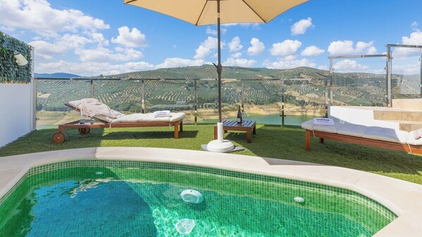 Ein Poolbereich mit Blick auf sanfte Hügel, zwei Liegestühle und ein Tisch mit einer Flasche und Gläsern.