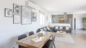 Una sala de estar moderna con comedor, sofás grises, una mesa de centro de madera y una cocina al fondo.