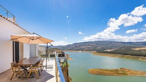 Eine Terrasse mit Tisch und Stühlen mit Blick auf einen See und eine hügelige Landschaft.