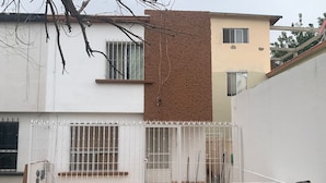 A two-story house with a white exterior, a brown section on the upper floor, and a fenced backyard with a patio table and chairs. - Consulado casa de Lujo (Ciudad Juárez)